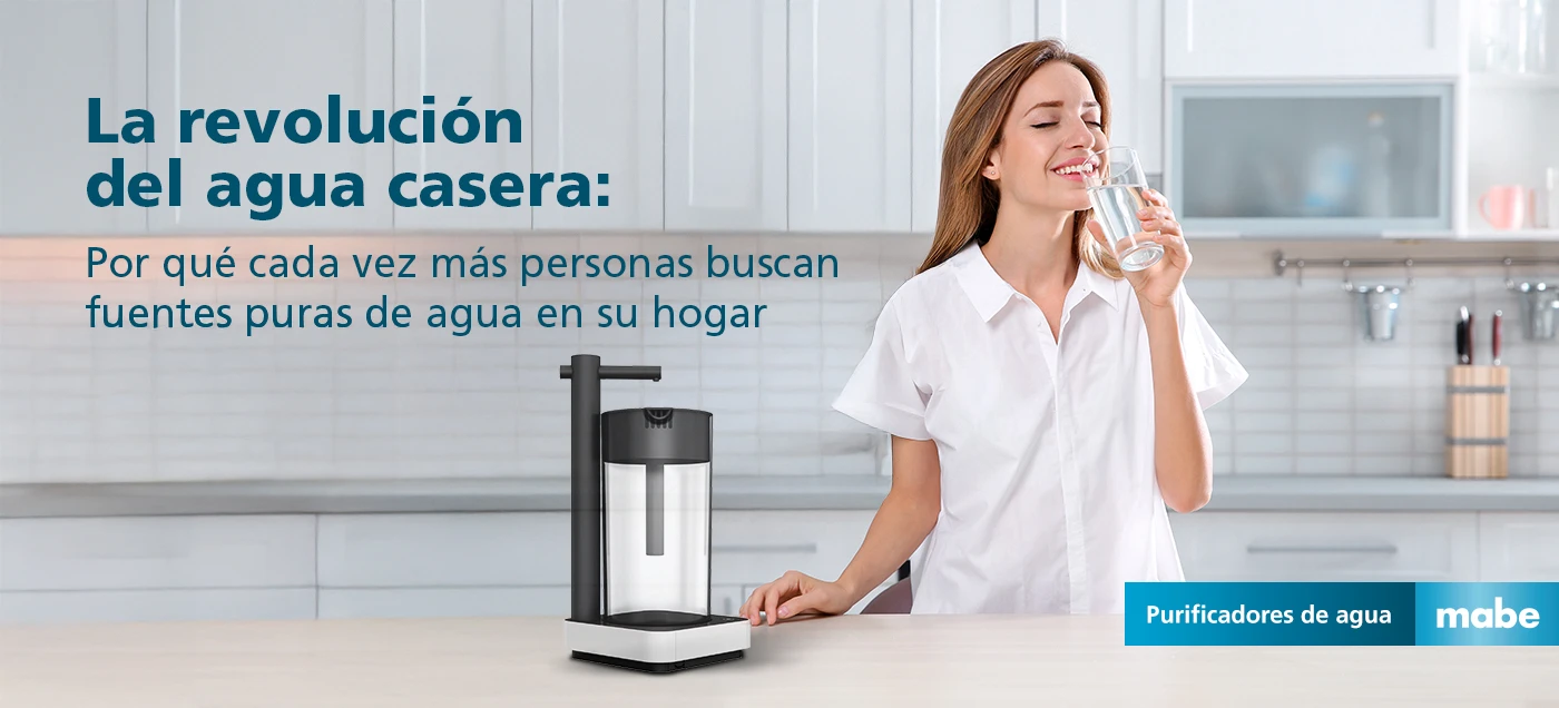 Mujer bebiendo agua junto a purificador mabe en cocina moderna, con el texto 'La revolución del agua casera: Por qué cada vez más personas buscan fuentes puras de agua en su hogar'. Campaña de purificadores de agua mabe