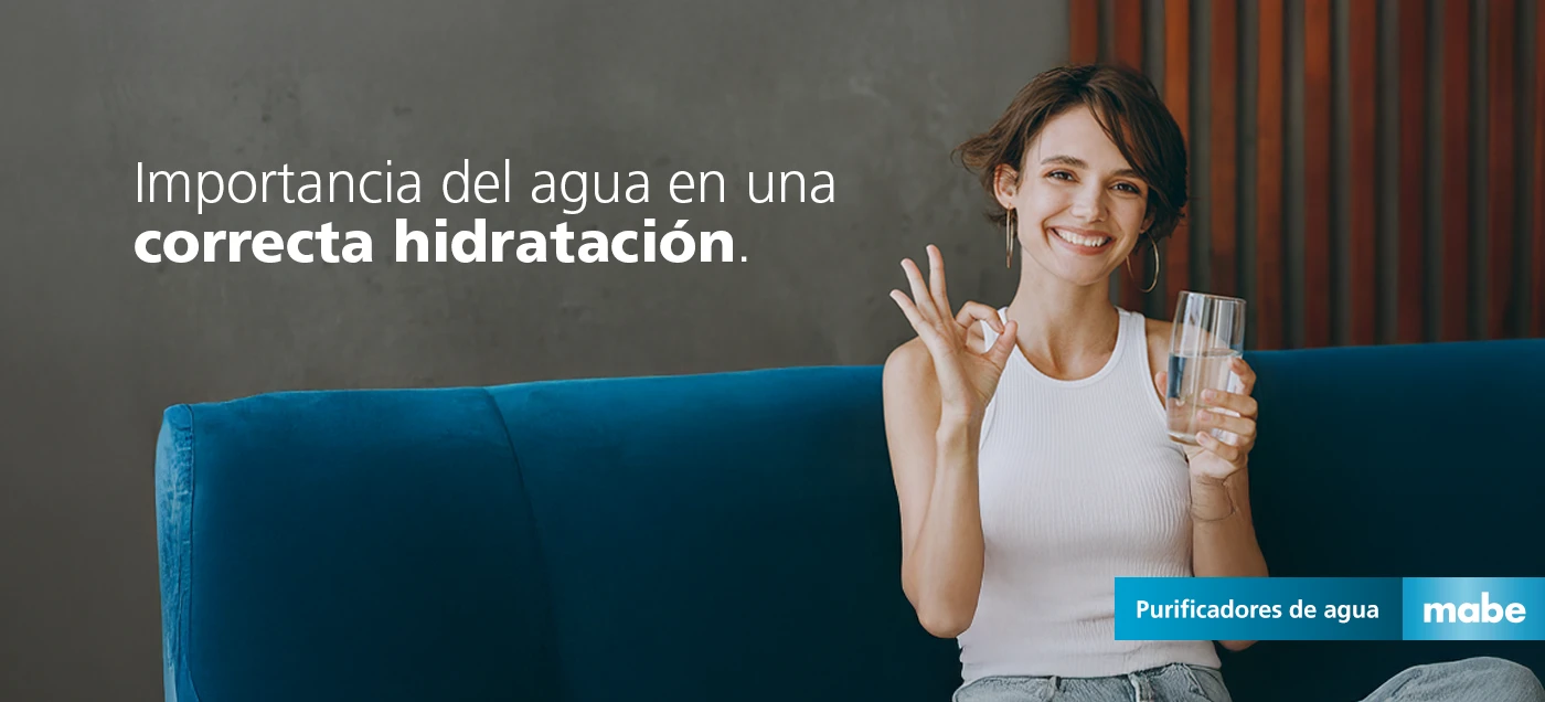 Mujer sonriendo y haciendo gesto de aprobación mientras sostiene un vaso con agua, junto al texto 'Importancia del agua en una correcta hidratación'. Campaña de purificadores de agua mabe